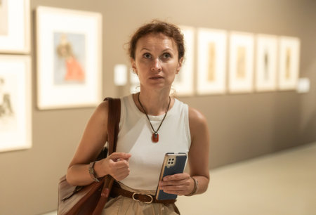 Woman with phone looking at art galleryの写真素材