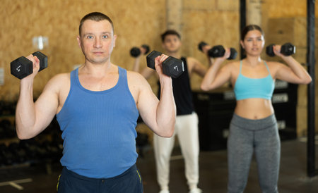Concentrated sporty man performing exercises with dumbbells in gymの写真素材