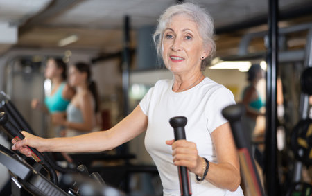 Slender athletic mature woman during cardio exercises on elliptical simulator in fitness centerの写真素材