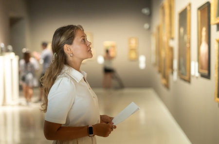 Woman with sheet piece of paper in hands view pictures and icons in museum hallの写真素材