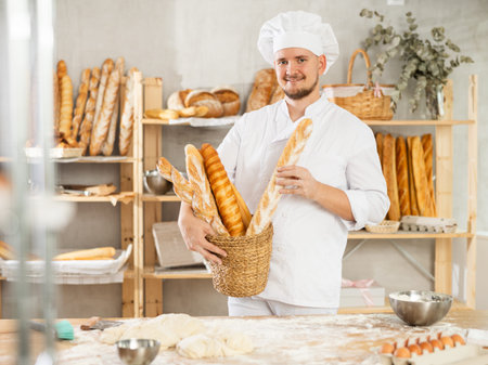 Male baker holds basket with finished products, shows many different baguettes