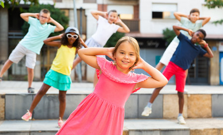 Positive girl dancing modern choreography with group of tweenagers outdoors