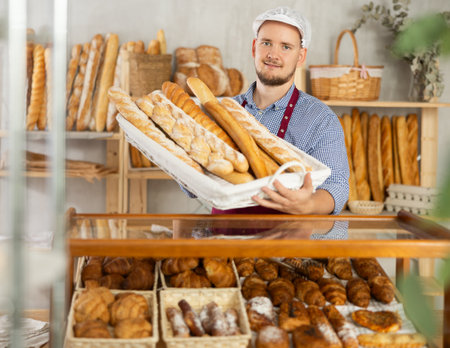 Portrait of smiling baker with fresh bread and baguettes at bakeryの写真素材