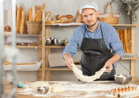 Professional baker prepares raw yeast dough in a bakery, shaping it into baguette