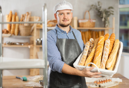 Male baker holds basket with finished products, shows many different baguettesの写真素材