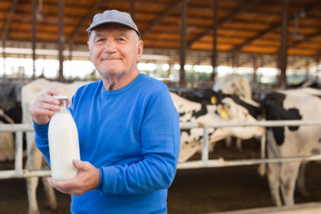 Farmer with bottle of milk in cowshedの写真素材