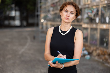 Portrait of female master of ceremonies funeral in black dress with a holder in her hands in columbariumの写真素材