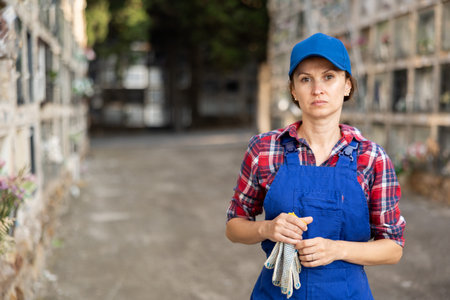 Young female cemetery employee stands with cloth work gloves in handsの写真素材