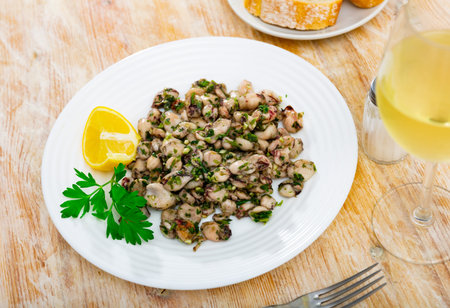 There are pieces of grilled squid on plate. Seafood is complemented with lemon and parsley