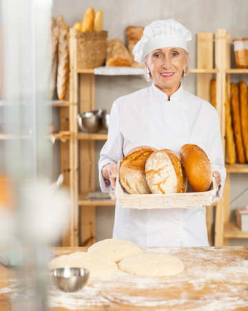 Portrait of female baker holding fresh rustic bread in her hands