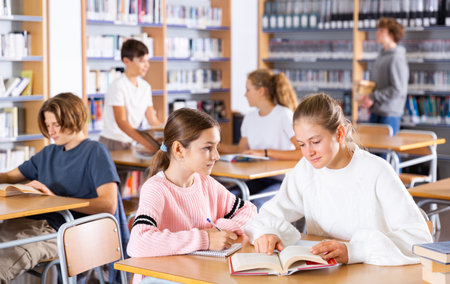 Two female friends reading books together and preparing for exams in school libraryの写真素材