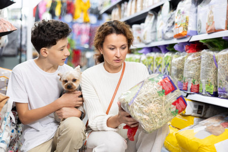Mom and boy with dog Yorkshire Terrier, take hay from shelf, in pet store.