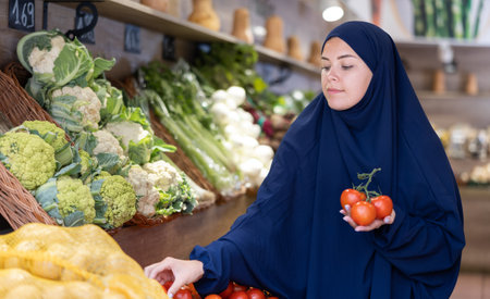 Young female shopper in muslim dress choosing tomatoes in supermarketの写真素材