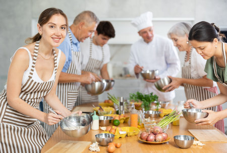 Positive young woman attendee of cooking course learning how to mix sauceの写真素材