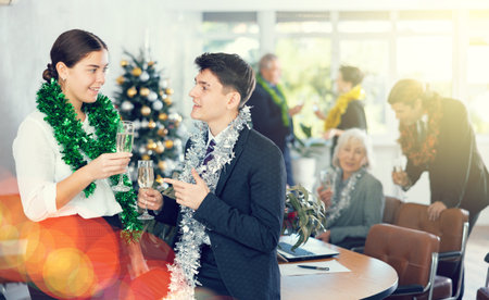 Two joyful male and female coworkers with tinsels and glasses of champagne during corporate New Year party in officeの写真素材