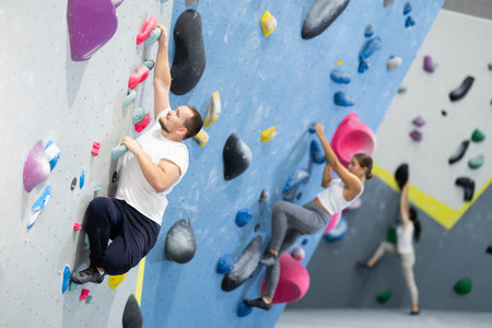 Man climbing a tall, indoor, man made rock climbing wall