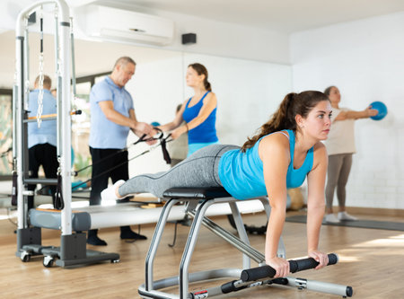 Young woman practicing pilates on pedal fitness chair in sports hallの写真素材