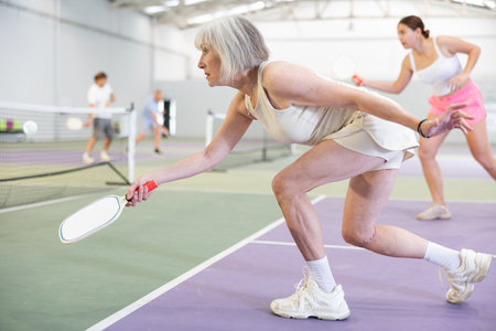 Positive elderly woman playing pickleball on indoor courtの写真素材