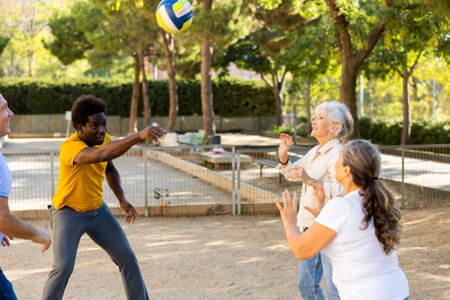 Joyful multiracial group of mature adult people playing volleyball game outdoorsの写真素材