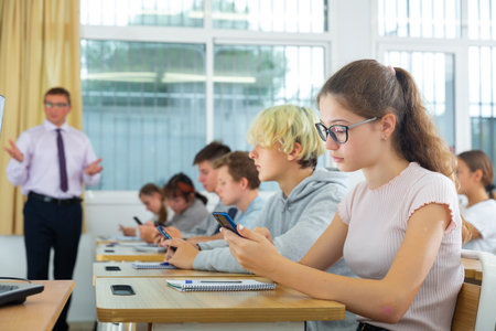 Teen students using social media on phones on lessonの写真素材