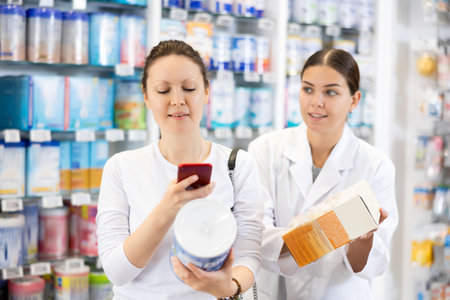 Female pharmacist helps female customer find baby formula from photo on internetの写真素材