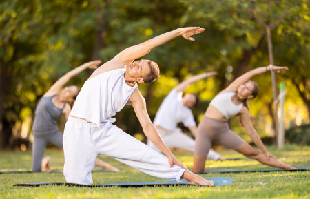Yoga lesson visitors with guy coach perform Parighasana in parkの写真素材
