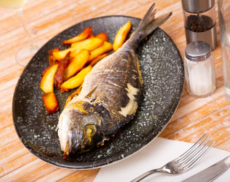 Baked dorada fish with vegetable garnish of fried potatoesの写真素材