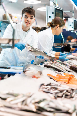 Smiling salesman demonstrating seabass in fish storeの写真素材