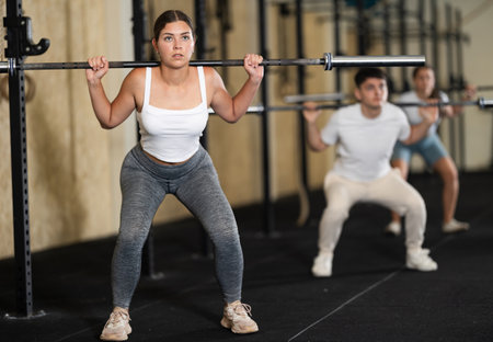 Girl in activewear exercising with barbell during group workout in gym centerの写真素材