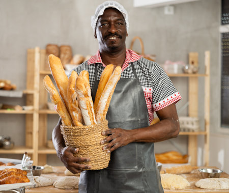 Portrait of experienced baker with tasty hot bread and baguettes in hands in kitchenの写真素材
