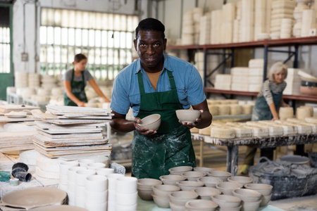 Portrait of african american man displaying cups at workshopの写真素材