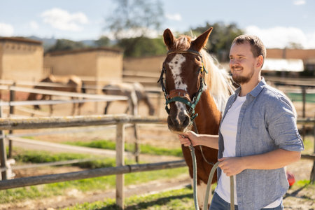 Happy man leading horse by bridle for walk in pasture