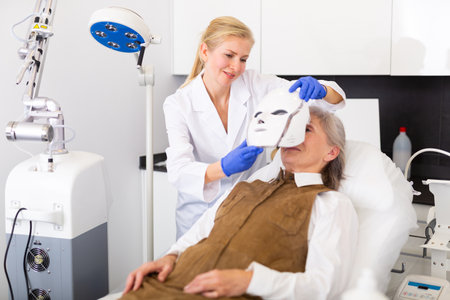 Cosmetologist using spectrum mask on elderly womanの写真素材
