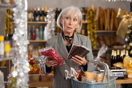Elderly woman chooses chocolates and candies in grocery