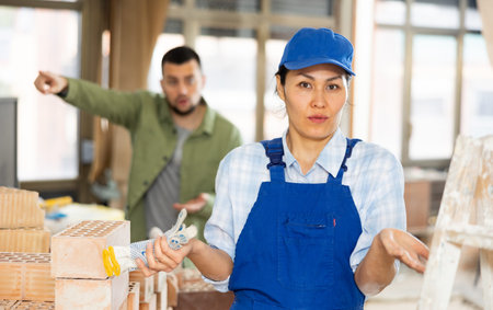 Confused female builder in building under construction with angry customer