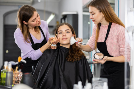 Two makeup artists apply makeup on the face of a young womanの写真素材