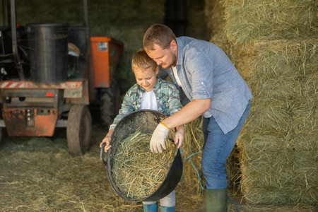 Boy helps his parents on horse farm - he carries basket of hay for horsesの写真素材