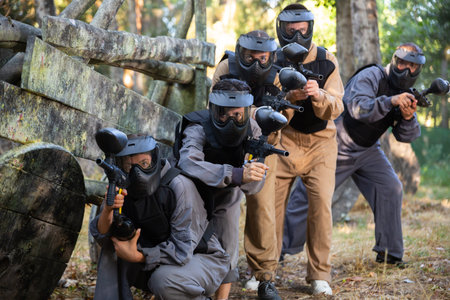 Group of paintball players aiming and shooting with guns outdoorsの写真素材