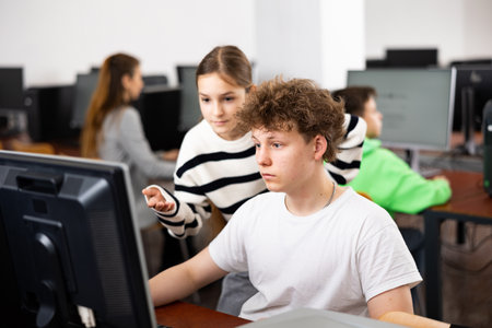 Teenage boy helping young girl with PC problem in computer classの写真素材