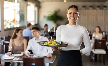 Waitress standing with salad and glass of wine on serving tray in restaurantの写真素材