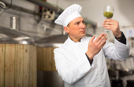 Experienced male brewer holding glass and looking at hops pellets