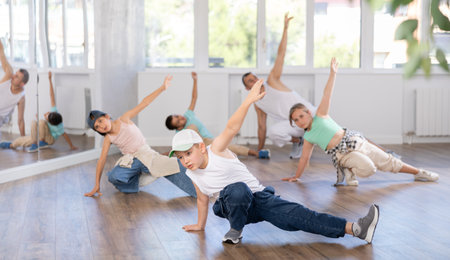 Happy emotional male teenager rehearsing popping techniques during group workout in modern street dance studioの写真素材
