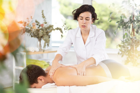 Adult woman giving back massage to young guyの写真素材