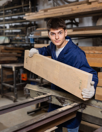 Young guy putting wooden board on cutting machineの写真素材