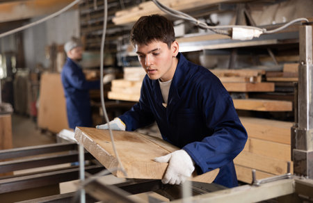 Young guy putting wooden board on cutting machineの写真素材