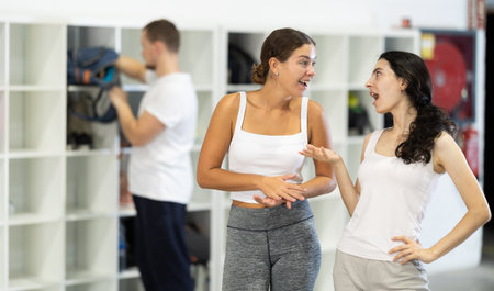 Two female climbers laughing and sharing stories in climbing gym locker room after exciting successful workoutの写真素材