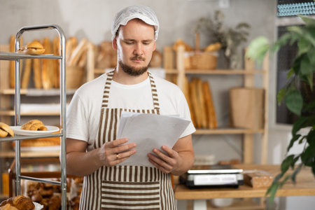 Young man seller reading document in bakery