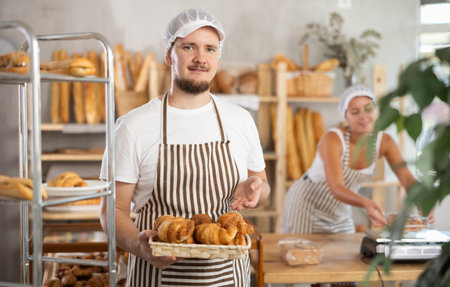 Young salesman displays croissants in square wicker basketの写真素材