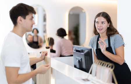 Female stylist stands near barbershop reception desk, communicates with male visitorの写真素材