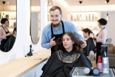 Young man barbershop employee stands next to female client, discussing details of haircutの写真素材